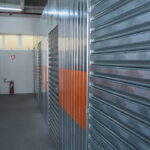 Corredor de boxes metálicos em unidade de self storage para estoque, mostrando espaço organizado e seguro para armazenamento de mercadorias.