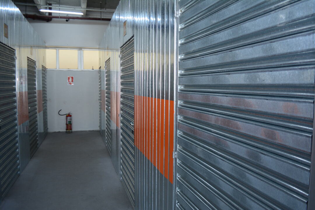 Corredor de boxes metálicos em unidade de self storage para estoque, mostrando espaço organizado e seguro para armazenamento de mercadorias.